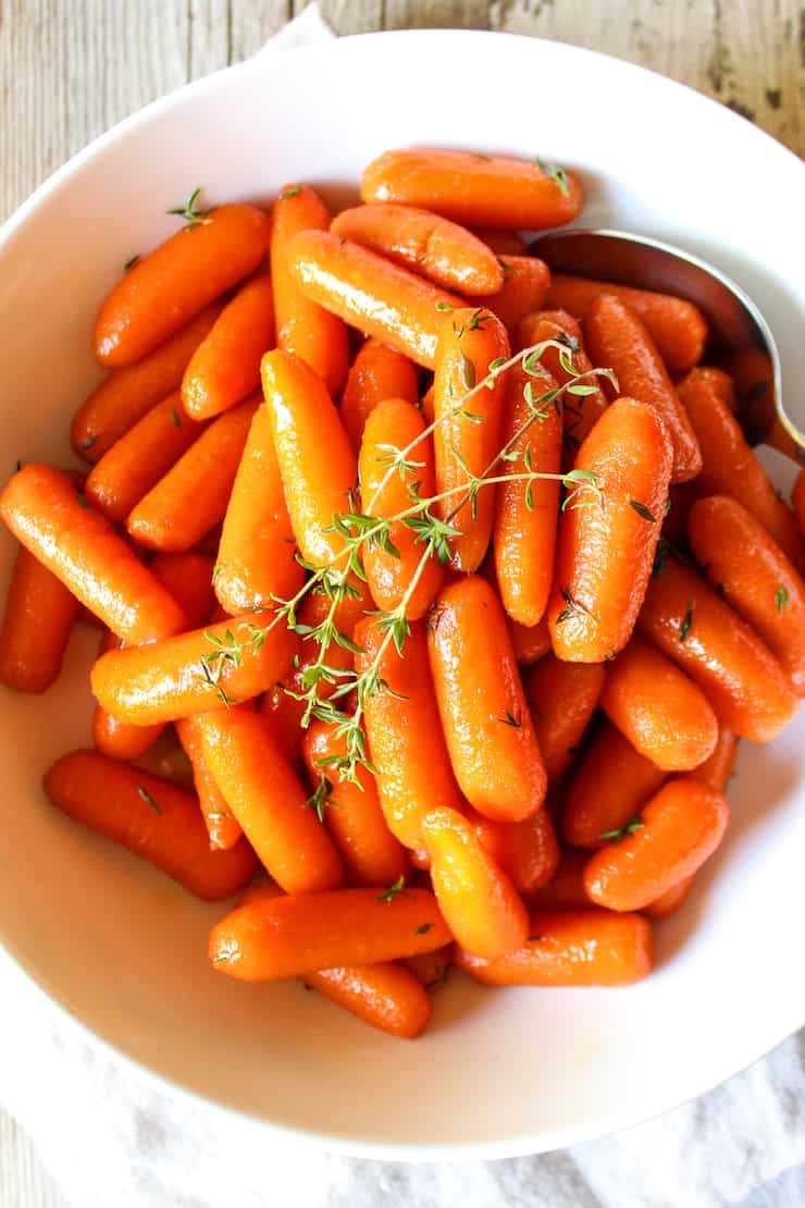 Honey brown sugar carrots in white serving bowl with fresh thyme.