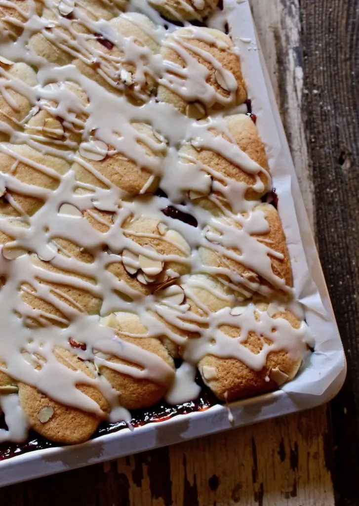 Cherry Pie Bars in pan drizzled with vanilla glaze and sliced almonds.