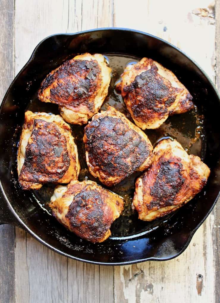 Overhead of cooked chicken thighs in skillet.