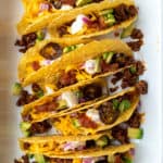 Beef tacos in hard shells in pan with toppings.