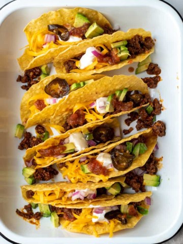 Beef tacos in hard shells in pan with toppings.