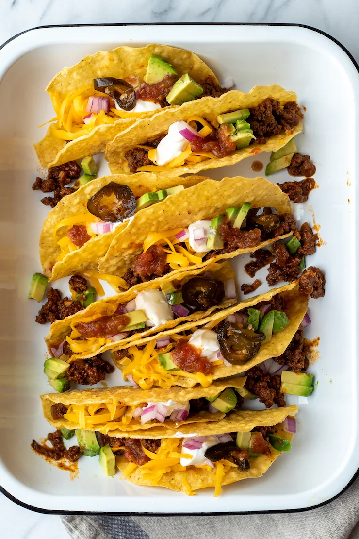 Beef tacos in hard shells in pan with toppings.