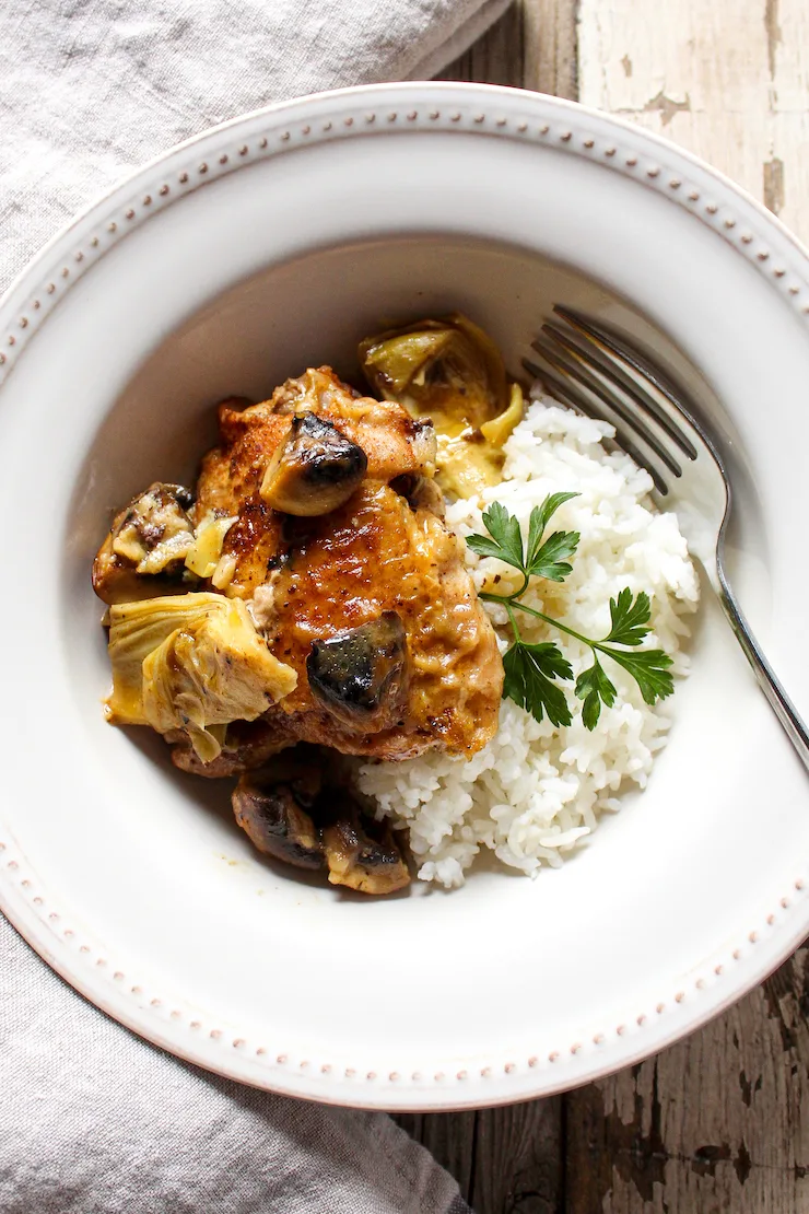 Plated serving of chicken and artichokes with rice and fork.