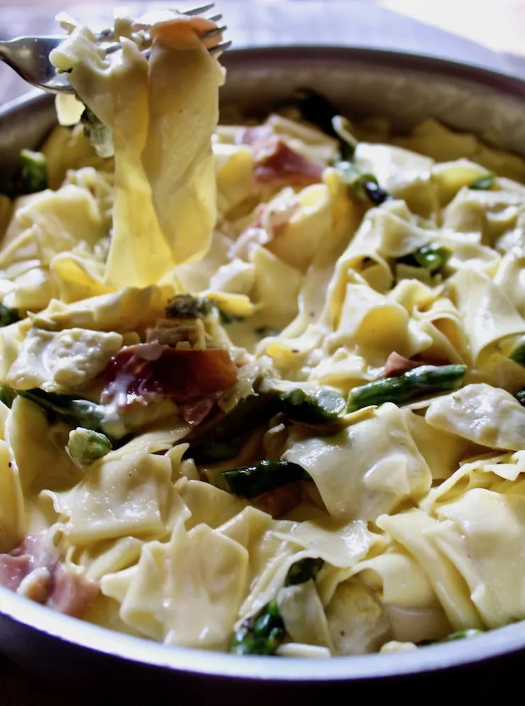 Pasta with Asparagus and Prosciutto in skillet with forkful of pasta above pan.