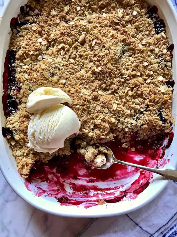 Fresh Blackberry Crisp in baking dish with ice cream and spoon.