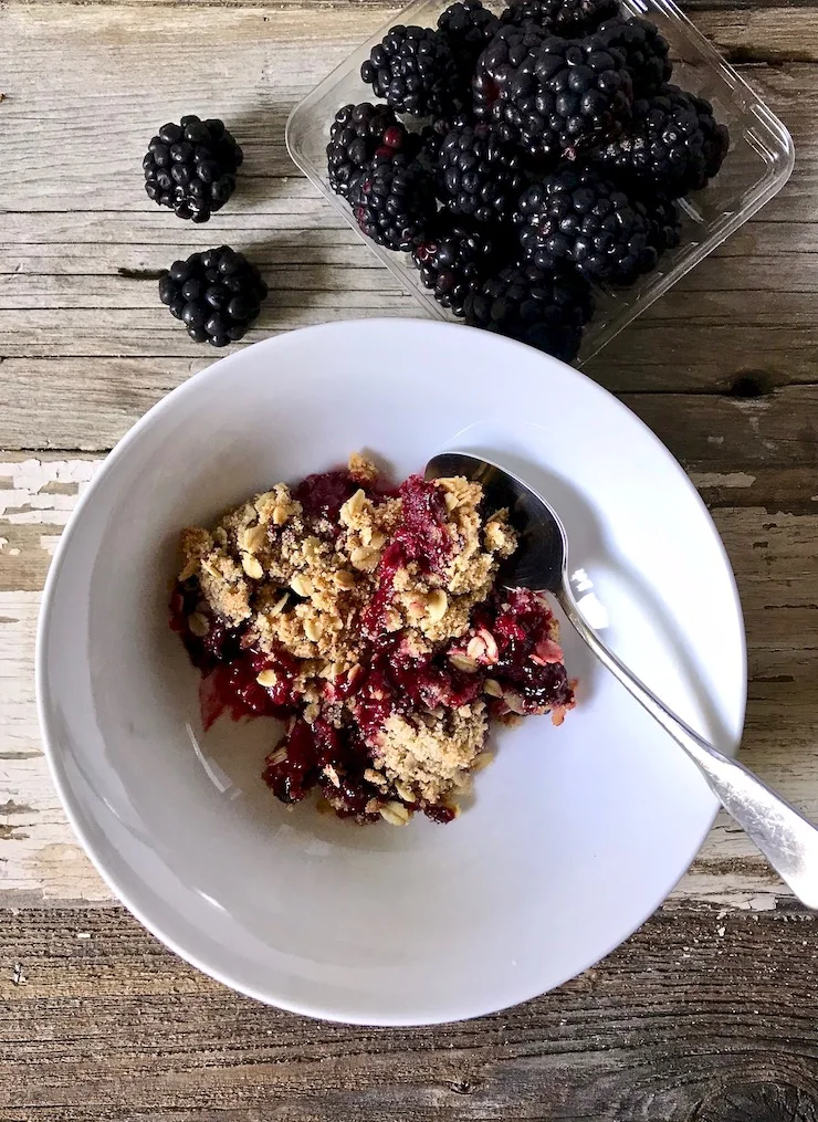 In bowl with spoon next to basket of blackberries