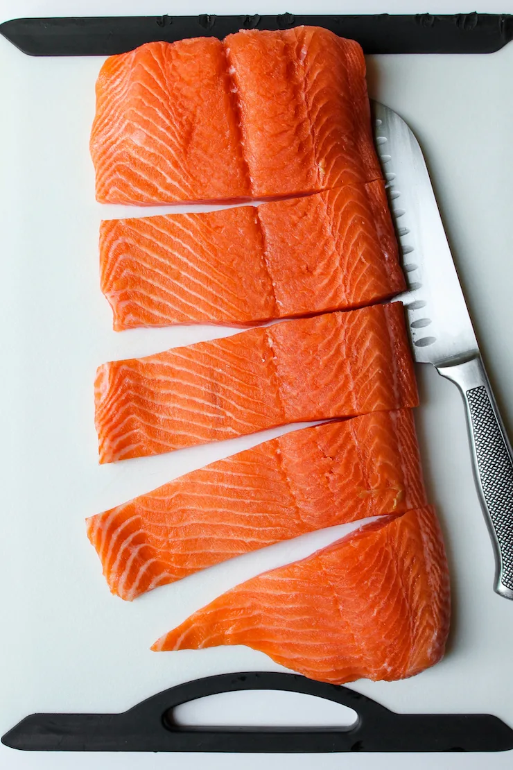 Large piece of salmon cut into portions on white board.