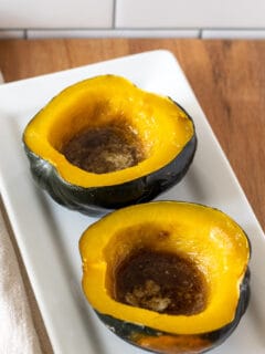 Baked acorn squash with butter and brown sugar on white platter.