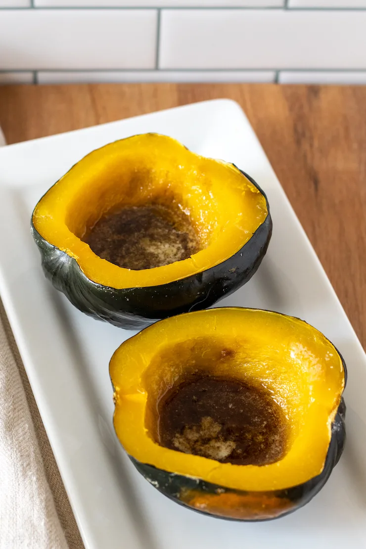 Baked acorn squash with butter and brown sugar on white platter.