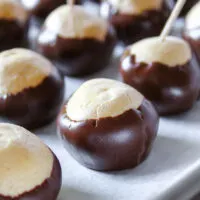 Buckeyes dipped in chocolate with tootpicks on parchment paper.