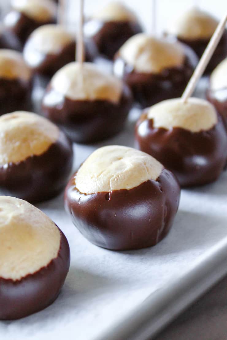 Buckeyes dipped in chocolate with tootpicks on parchment paper.
