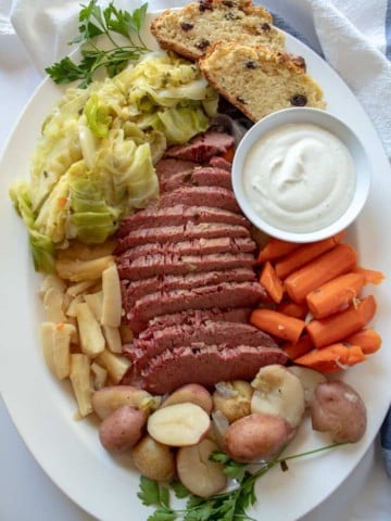 Instant Pot Corned Beef and Cabbage, arranged on platter with horsereadish sauce and Irish soda bread.