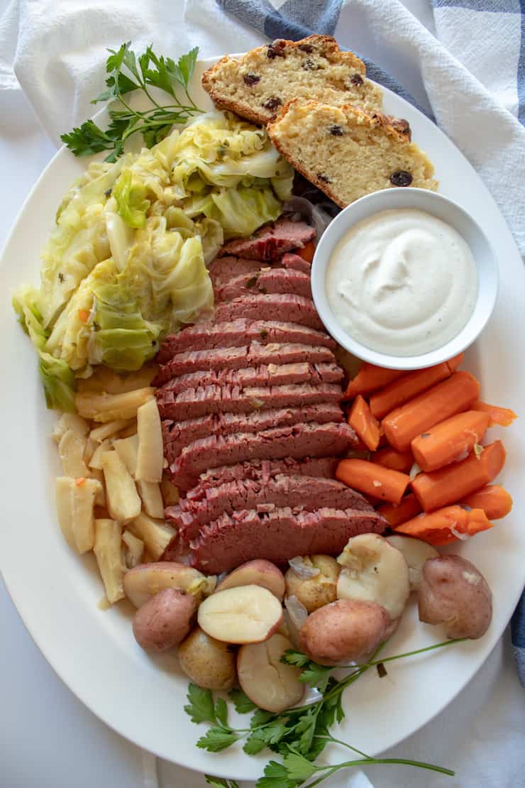 Instant Pot Corned Beef and Cabbage, arranged on platter with horsereadish sauce and Irish soda bread.