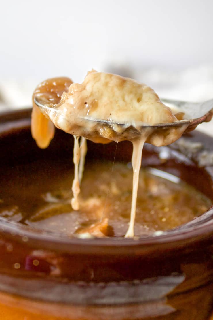 Close up of French onion soup on spoon with melted cheese.