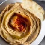 Hummus in white bowl with pita bread.