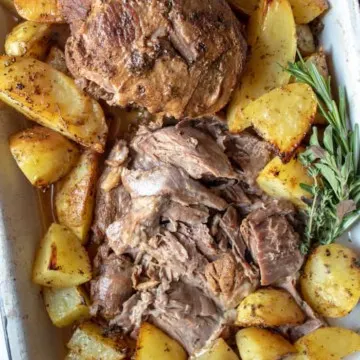Greek Instant Pot Leg of Lamb, sliced and arranged in pan, surrounded with Greek potatoes.
