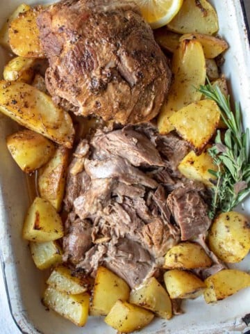 Greek Instant Pot Leg of Lamb, sliced and arranged in pan, surrounded with Greek potatoes.
