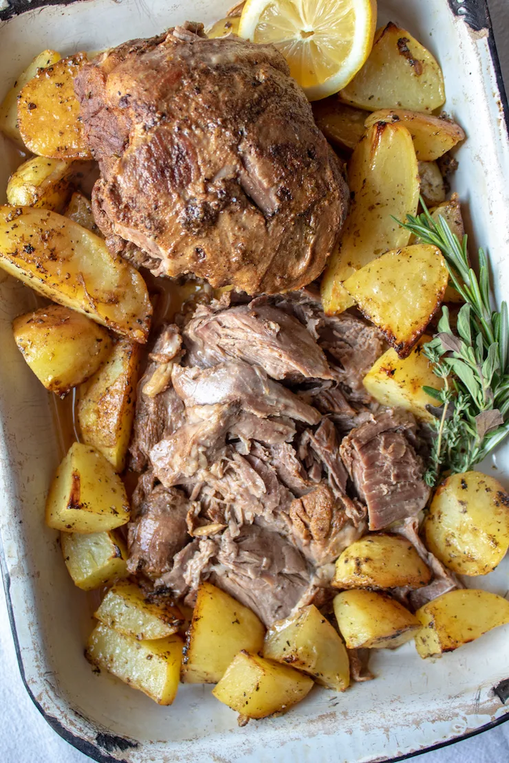 Greek Instant Pot Leg of Lamb, sliced and arranged in pan, surrounded with Greek potatoes.