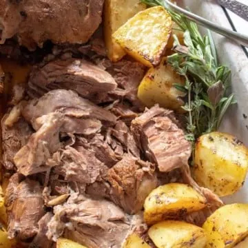 Greek Instant Pot Leg of Lamb, close up in pan with roasted potatoes.