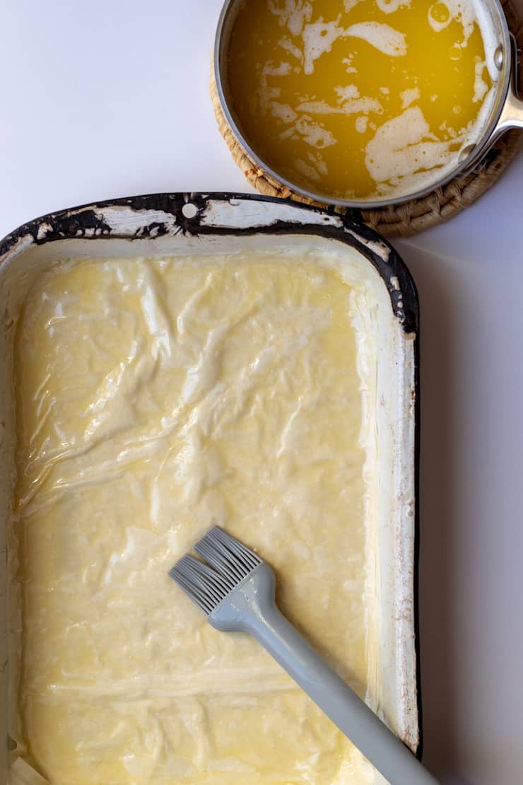 Layering phyllo sheets with melted butter.