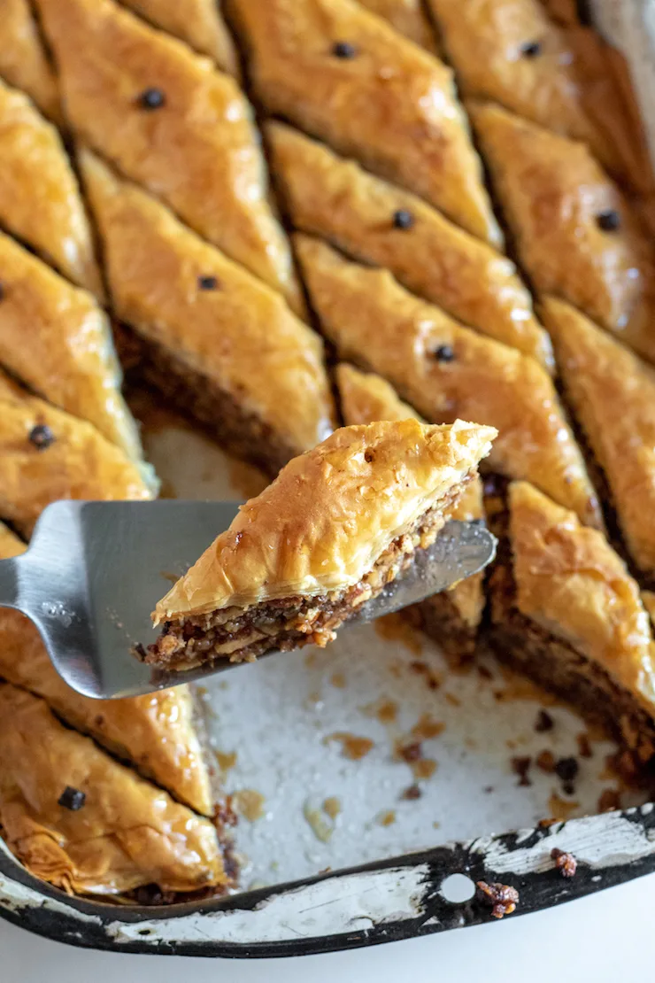 Greek baklava on serving knife above pan.