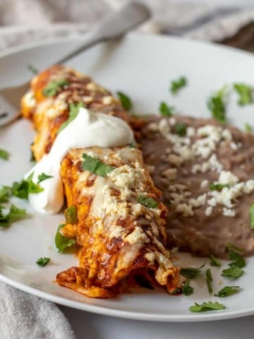 Enchilada on white plate with refried beans.