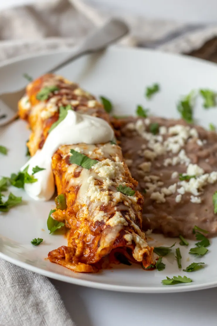 Enchilada on white plate with refried beans.