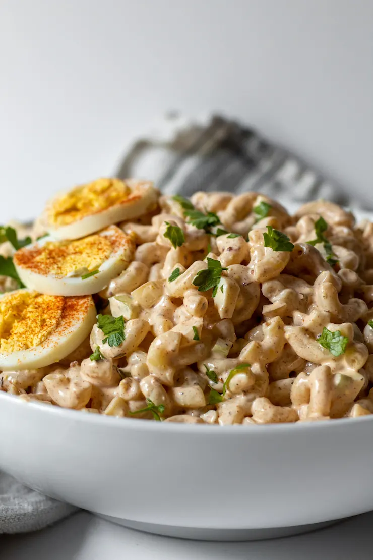 Sideview of macaroni salad heaped in white serving bowl.