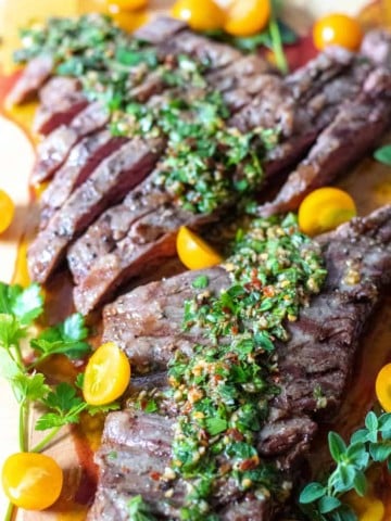 Sliced steak on cutting board with chimichurri and tomatoes.