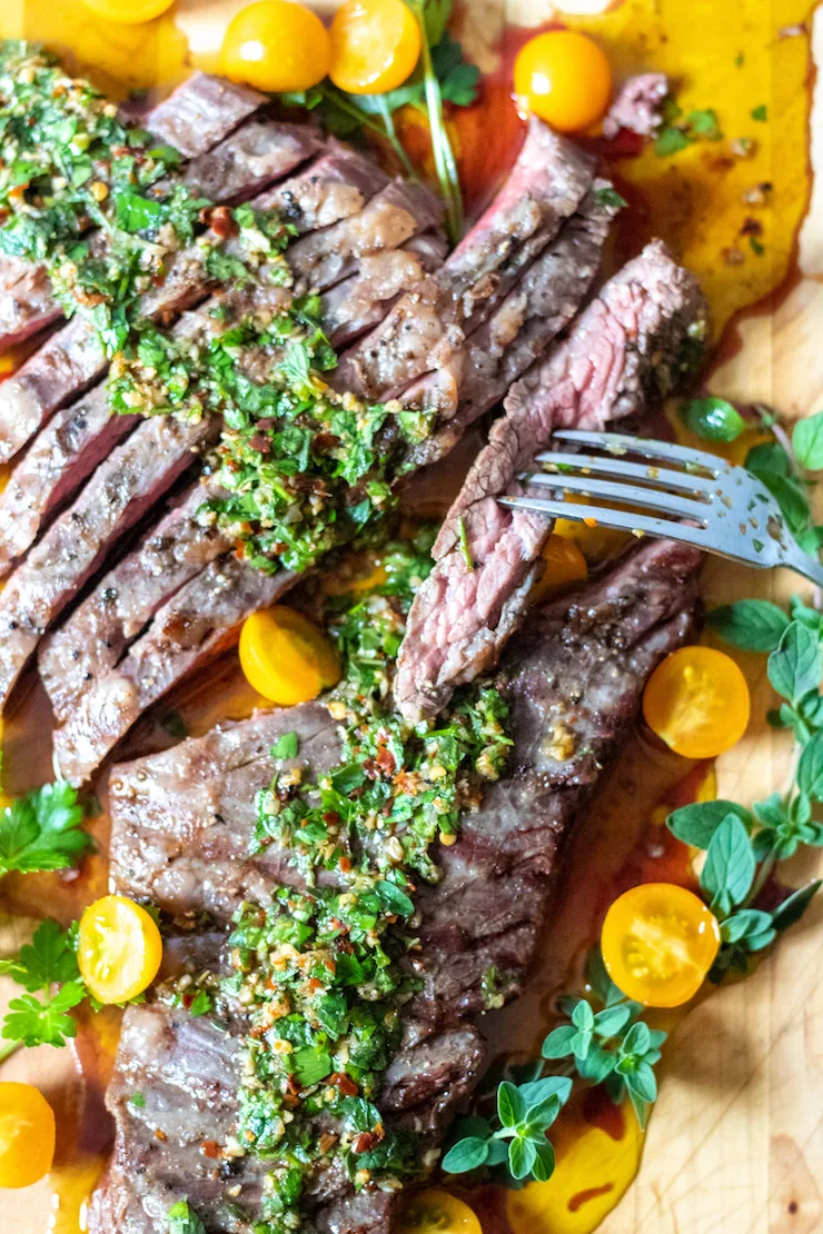 Overhead of steak with chimichurri and tomatoes with close up on fork.