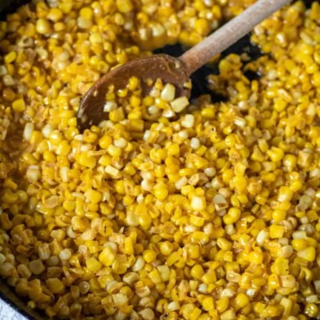 Cajun fried corn in cast iron skillet with wooden spoon.