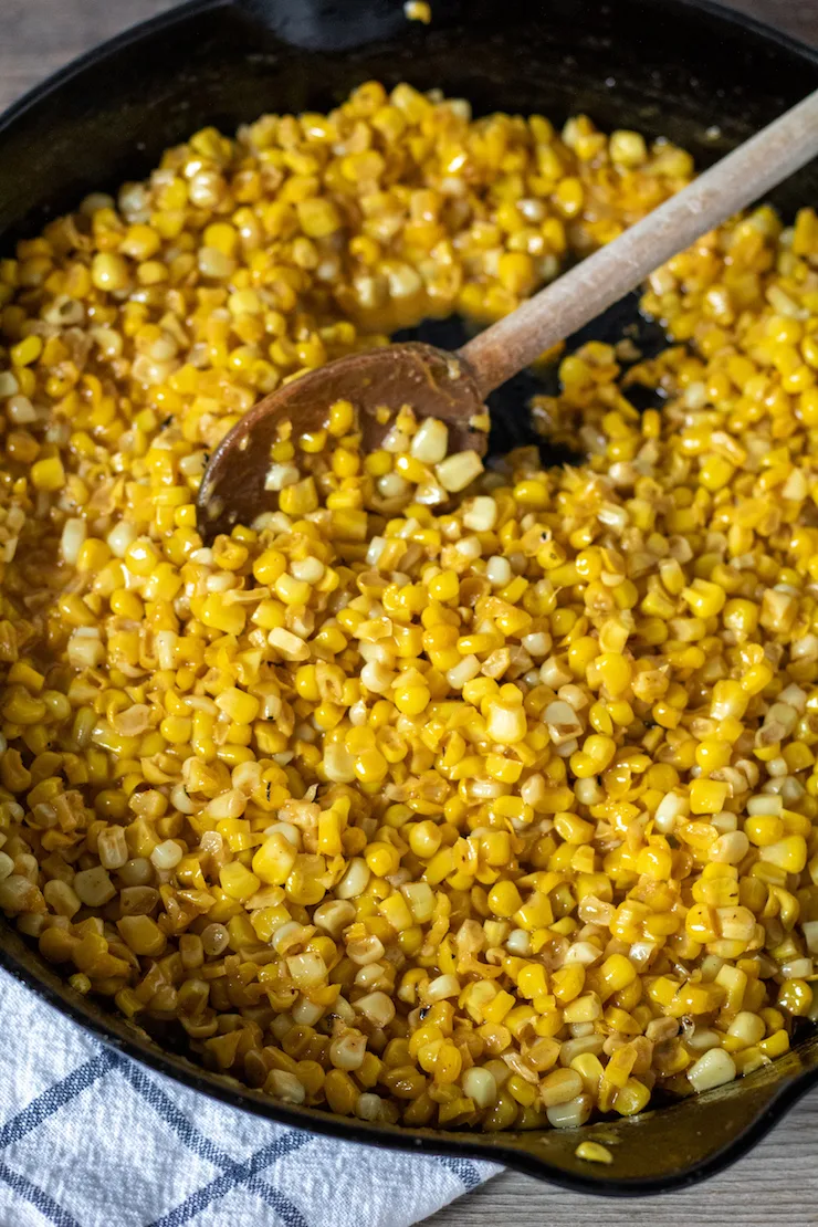 Cajun fried corn in cast iron skillet with wooden spoon.