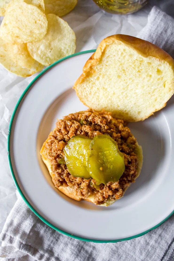 Overhead view of open faced turkey sloppy joe with pickles and potato chips