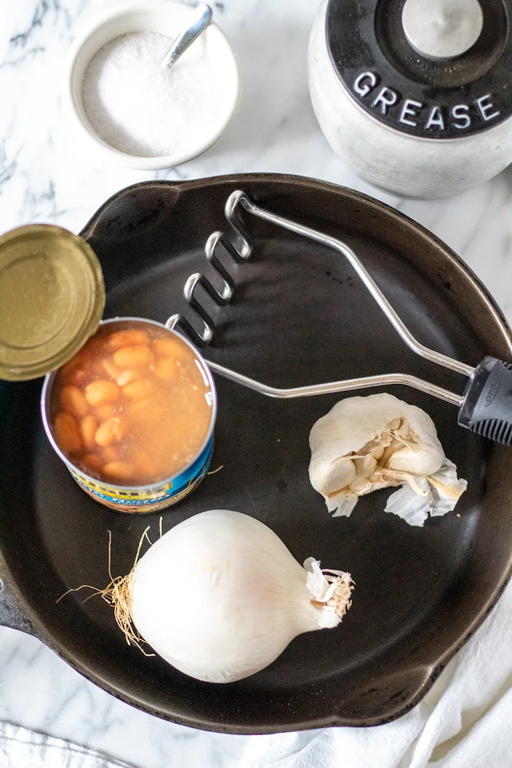 Ingredients, potato masher and cast iron skillet.