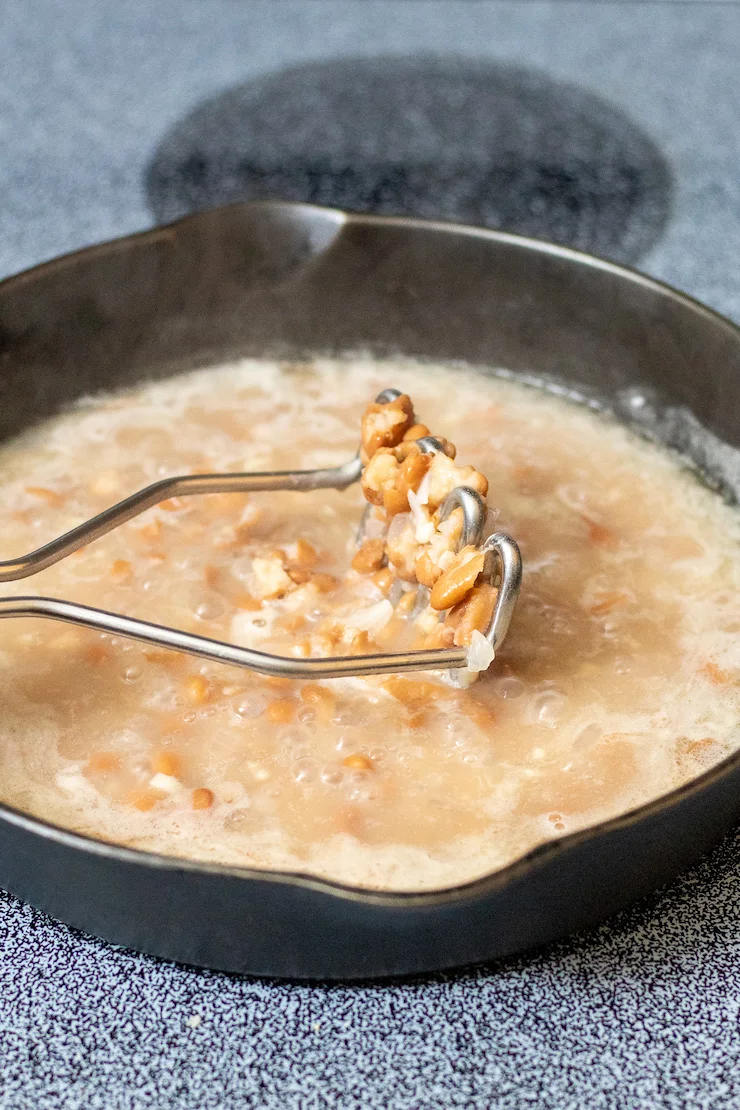 Potao masher in skillet with beans mixture.