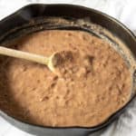 Refried beans in cast iron skillet with wooden spoon.