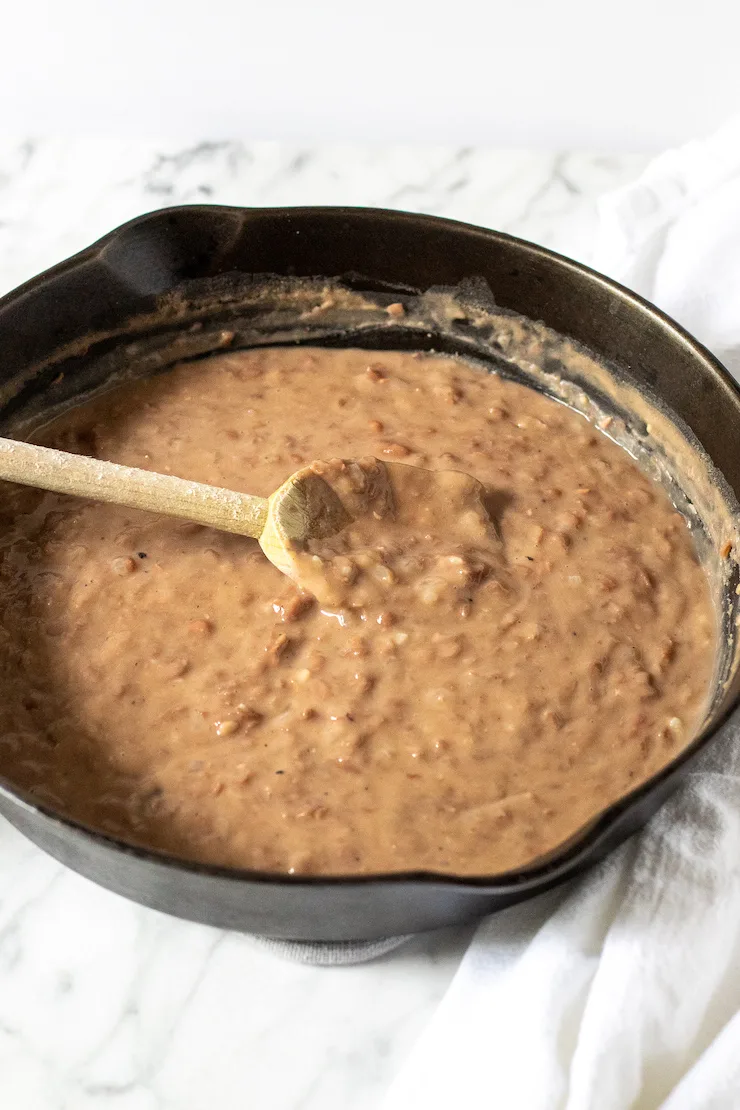 Refried beans in cast iron skillet with wooden spoon.