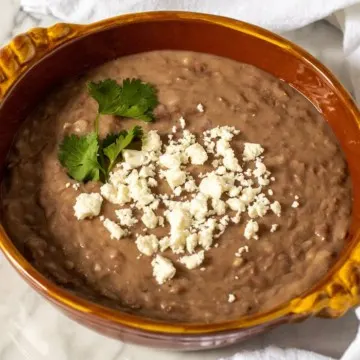 Refried beans in serving dish with queso fresco.