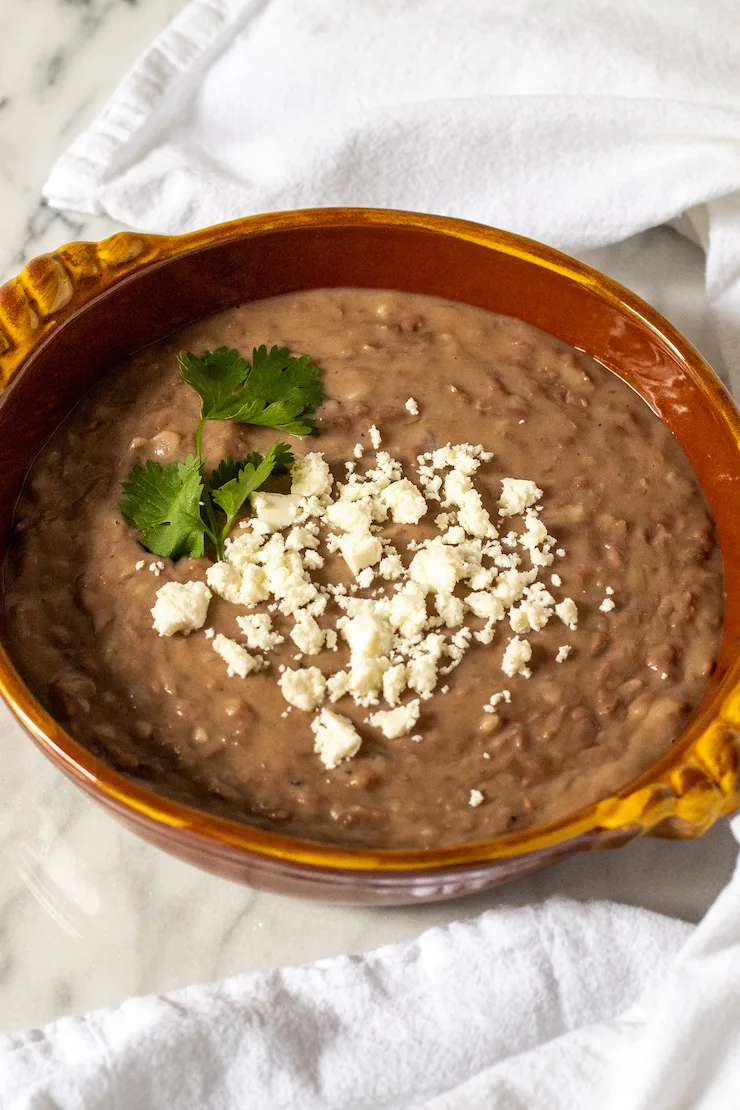 Refried beans in serving dish with queso fresco.