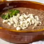 Refried beans in serving dish with queso fresco.