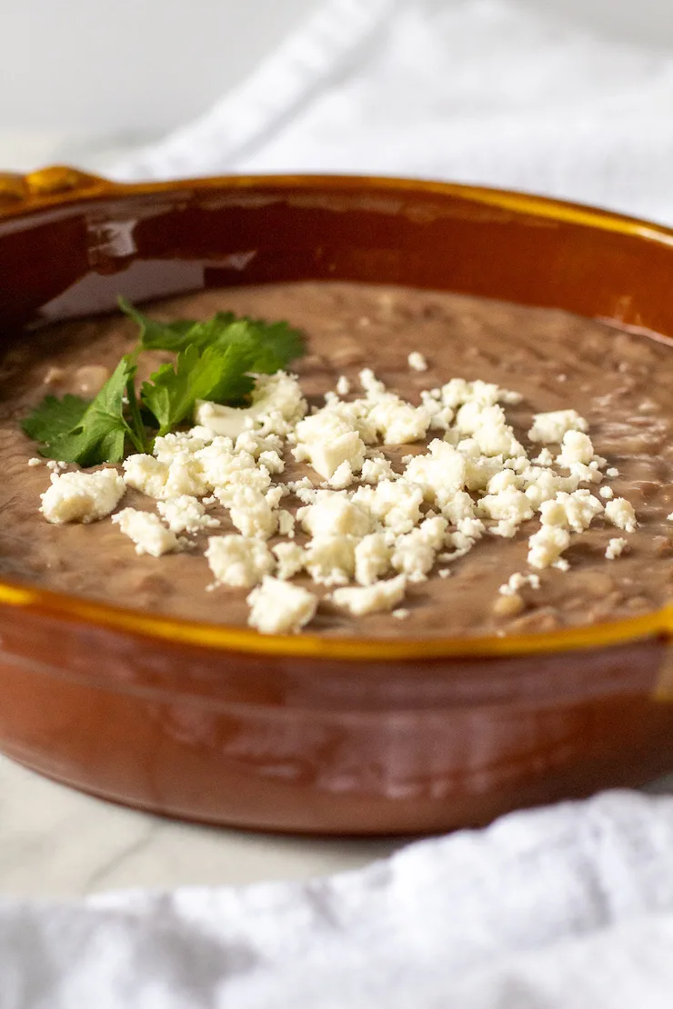 Refried beans in serving dish with queso fresco.