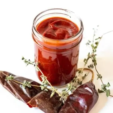 Enchilada sauce in jar surrounded by dried chiles and oregano.