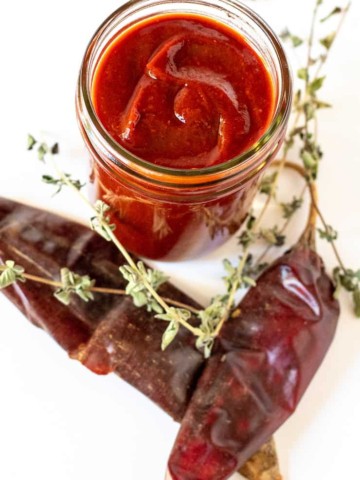 Enchilada sauce in jar surrounded by chiles and oregano.