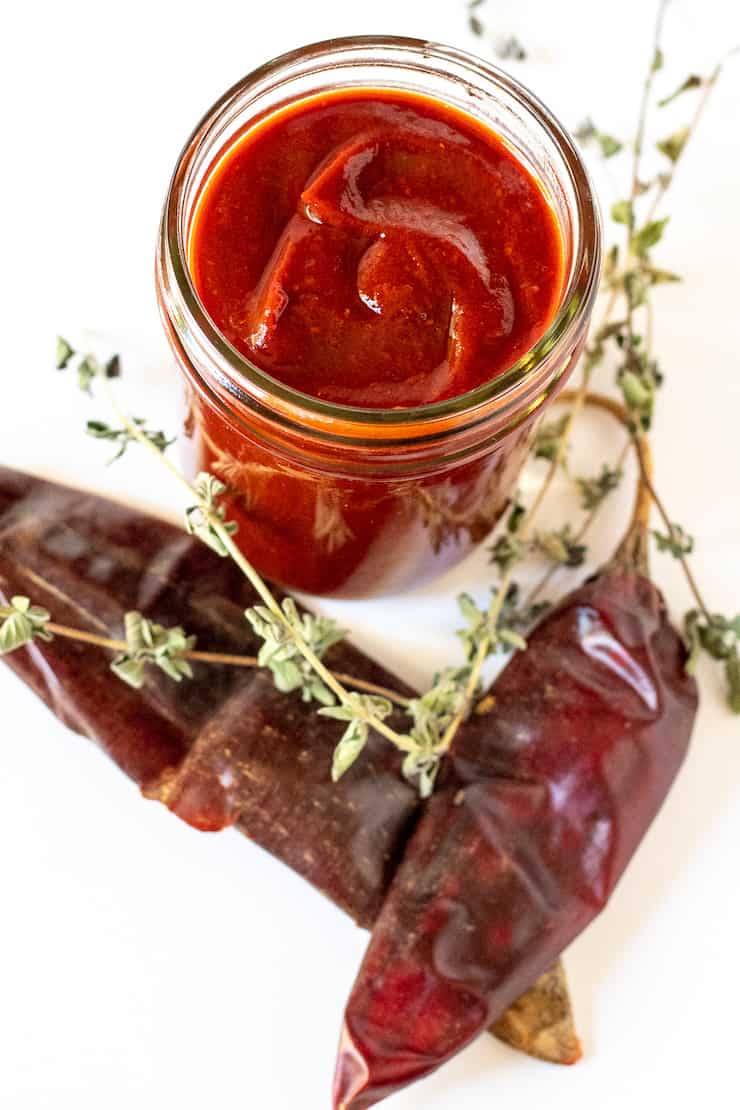 Enchilada sauce in jar surrounded by chiles and oregano.