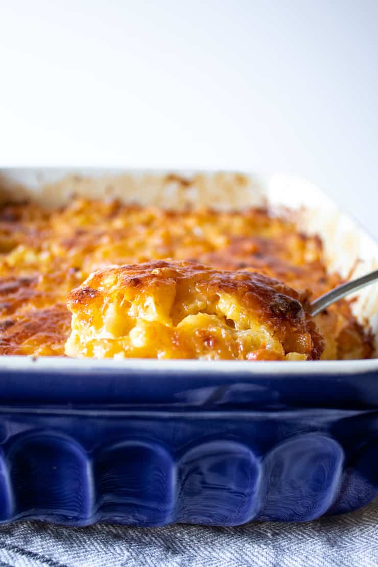 Serving of baked macaroni and cheese on spoon pulling out of baking dish.