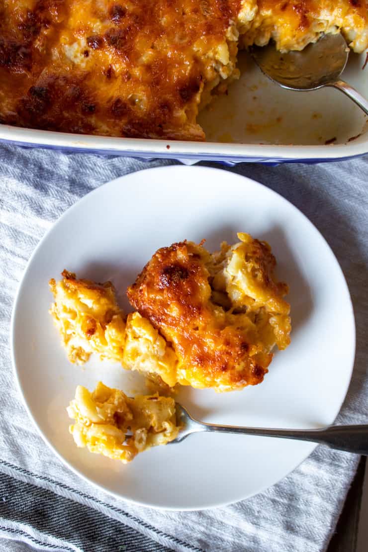 Serving of mac and cheese on white plate with casserole in background.