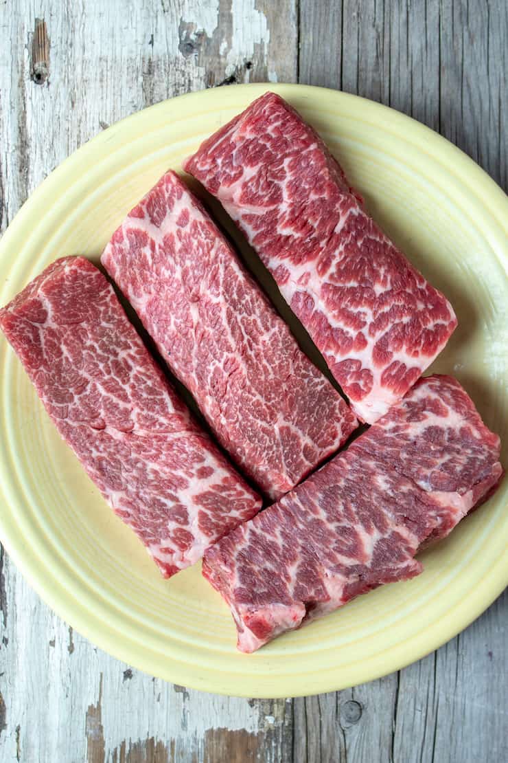 Uncooked boneless beef short ribs on plate.