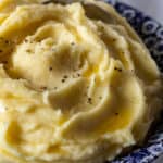 Finished mashed potatoes in bowl with drizzled melted butter and pepper.