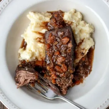 Short ribs plated with mashed potatoes and sauce, showing forkful of beef.