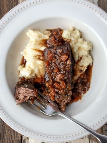 Short ribs plated with mashed potatoes and sauce, showing forkful of beef.
